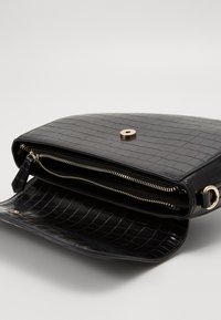 Svart krokodilpräglad läderhandväska med magnetstängning, en zippered ficka och detaljer i guldton.