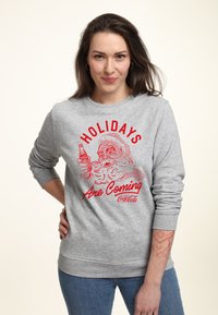 Felpa grigia con una grafica rossa di Babbo Natale che tiene una bibita, con la scritta "Le FESTE stanno arrivando" in stile vintage. Materiale misto cotone.
