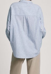 Light blue and white striped oversized shirt with a back pleat, buttoned cuffs, and a folded collar. Made of soft fabric.
