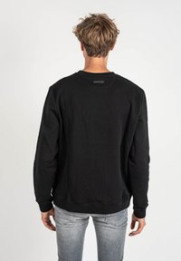 Sudadera negra con cuello y puños acanalados, de corte holgado y textura suave, combinada con jeans gris claro.