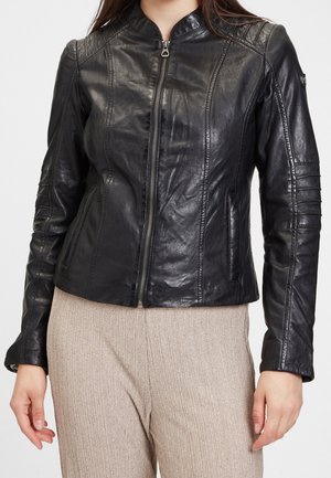 Femme portant une veste en cuir noire cintrée avec une fermeture éclair à l'avant et des surpiqûres matelassées sur les épaules et les manches.