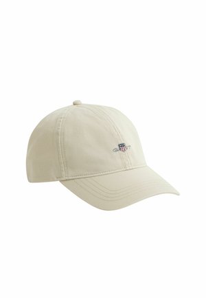 Casquette de baseball beige avec visière incurvée et petit logo brodé affichant un bouclier et le texte "GANT" sur le panneau avant gauche.