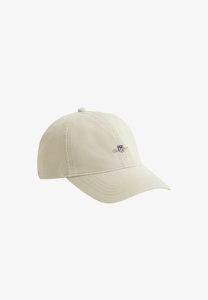 Casquette de baseball beige avec visière incurvée et petit logo brodé affichant un bouclier et le texte "GANT" sur le panneau avant gauche.
