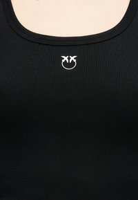 Μαύρο τοπ από ριμπ ύφασμα με τετράγωνο ντεκολτέ που διαθέτει μικρό λευκό κεντητό σχέδιο δύο πουλιών που κοιτάζουν το ένα το άλλο.