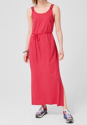 Femme portant une robe maxi sans manches rayée rouge et blanche avec une taille à cordon et des baskets multicolores, debout sur un fond gris.