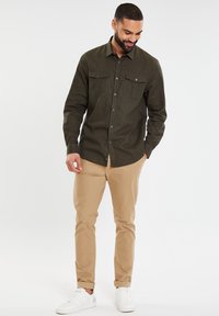 Olijfgroene button-up overhemd met twee borstzakken, gedragen met beige chino's en witte sneakers. Het overhemd heeft een kraag en aansluitende mouwen.