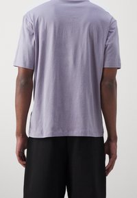 Lilla bomulds t-shirt med korte ærmer, afslappet pasform, rund halsudskæring og ensartet tekstur. Bagudsigten viser ingen grafik eller logoer.