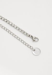 Bracciale argento con cristalli trasparenti e rotondi incastonati in metallo, collegato da una catena, con chiusura a molla e un'etichetta a forma di cerchio.