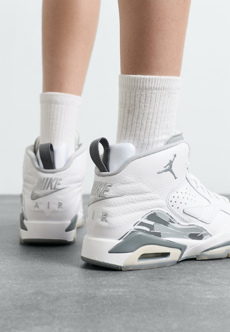 Hvite lær sneakers har et grått aksent på sålen, fremtredende hæltab, perforerte paneler og en "Nike Air"-logo på baksiden.
