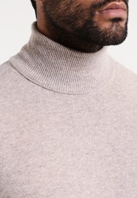 Ljusbeige polotröja gjord av ett mjukt, strukturerat stickat tyg, med ribbat krage och sömlös design.