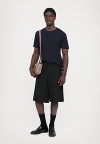 Marine T-skjorte, svarte knelengde shorts, svarte sokker og lærsko. Har også en liten beige crossover-veske. Enkelt design, uten mønstre.