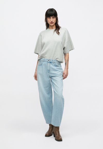 T-shirt gris surdimensionné à manches courtes associé à un jean large bleu clair et des bottines marron. Tissu lisse et coupe décontractée.