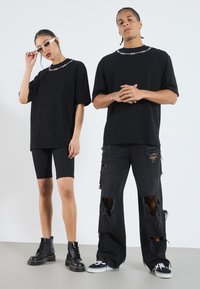 Camisetas oversized negras con diseño de alambre de espino, combinadas con pantalones cortos de bicicleta negros y pantalones negros desgastados; los accesorios incluyen botas negras y gafas de sol.