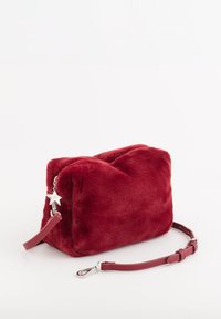 Bolso de hombro de felpa roja con forma rectangular, cuenta con una correa de cuero roja desmontable, un charm plateado en forma de estrella y una textura suave.