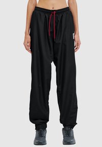 Czarne, lekkie, luźne spodnie z elastycznym pasem, czerwonym sznurkiem i elastycznymi mankietami. Posiadają małą naszywkę z logo z boku.