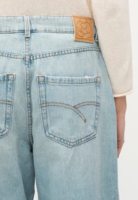 Γαλάζια τζιν παντελόνια από ντένιμ σε όψη από πίσω με ραμμένες τσέπες και φυσαρμόνικα από δέρμα ταμπά στη ζώνη μέσης, φορεμένα με κρεμ πλεκτό τοπ.