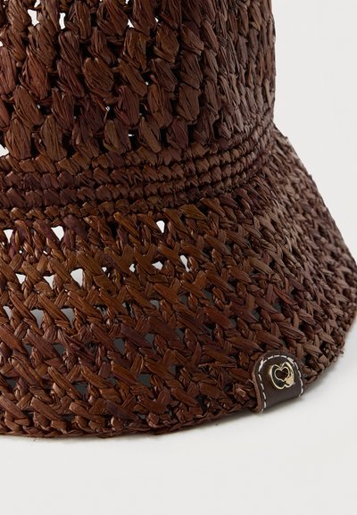 Chapeau de soleil en paille tressée marron avec large bord et petite étiquette en cuir présentant un logo en forme de cœur sur le bord.