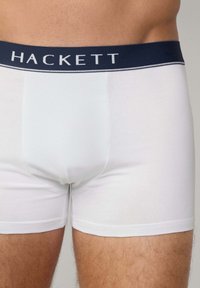 Boxer in bianco con elastico blu navy, con il logo "HACKETT" in bianco. Tessuto morbido e liscio con un design aderente.