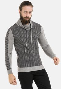 Grau- und schwarzer Strickpullover mit einem strukturierten Muster, Kragen im Cowl-Design und langen Ärmeln. Verfügt über kontrastierende, gemusterte Abschnitte und Kordeln.
