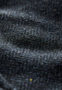 Gros plan d'un tissu en laine gris foncé texturé avec des fibres visibles et une surface douce légèrement duveteuse.