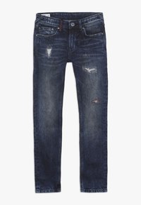 Tmavé denimové džíny s úzkým střihem, které mají poškozené detaily včetně roztržených záplat a klasického pětikapsového designu.