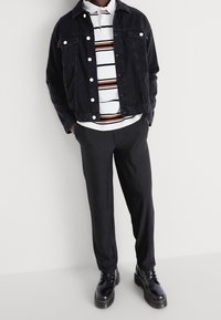 Zwarte denimjas met witte hardware over een gestreepte polo. Donkere, gestructureerde broek en zwarte veterschoenen maken de outfit compleet.