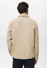 Beige lærredjakke med klassisk krave, knappede manchetter, lige snit og minimale syninger, med et rygparti design.