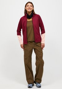 Maronfarvet og lyserød zip-up jakke, brun bluse, grøn cargo-bukser og blå træningssko. Har sporty design og flere lommer.