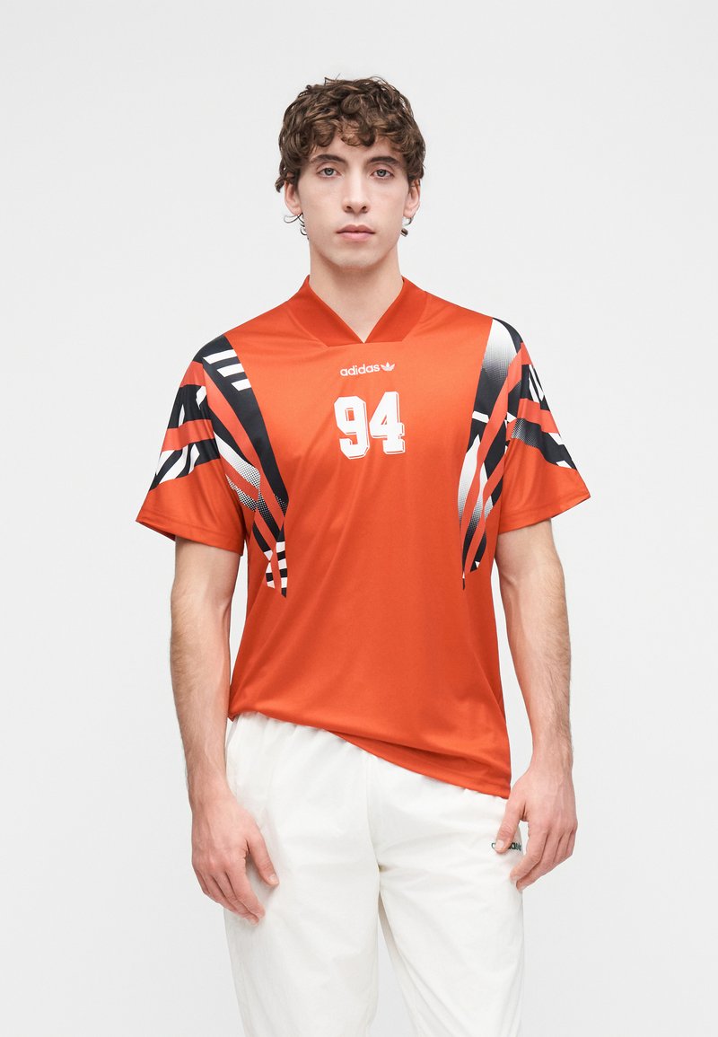 Maillot de sport orange avec des bandes graphiques noires et blanches, manches courtes, et le numéro 94 imprimé en évidence sur le devant.