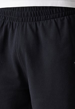 Shorts de sport noirs en tissu texturé, avec une ceinture élastique et un petit logo sur le côté.