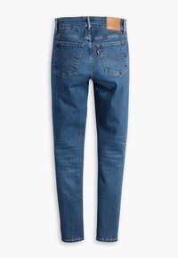 Jean en denim bleu à coupe droite, avec un patch en cuir de marque, deux poches arrière et un léger effet froissé sur le tissu.