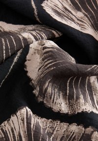 Patterned fabric featuring a black background with large, abstract beige and brown shell designs, highlighting textural lines and shapes.