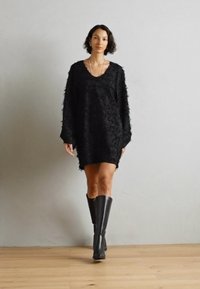 Vestido de punto negro oversized con un patrón floral texturizado, que presenta mangas largas y un escote en V profundo. Combinado con botas negras hasta la rodilla.