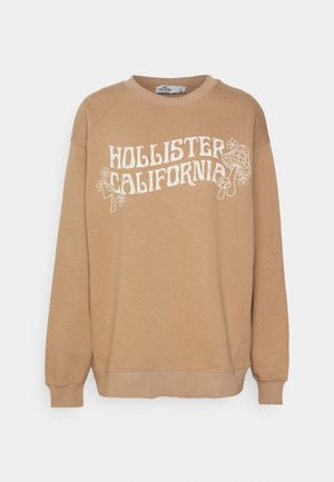 Beige sweatshirt i mjukt tyg med rund halsringning och raglanärmar. Framsidan har vit text och lekfulla grafiska element.