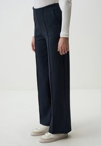 Marineblau gestreifte weite Hosen mit hohem Bund, glatter Textur und seitlichen Taschen, getragen mit weißen Turnschuhen.