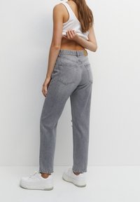 Jean gris taille haute avec une coupe décontractée, ourlet effiloché, design à cinq poches et une étiquette en cuir marron clair sur la ceinture arrière.