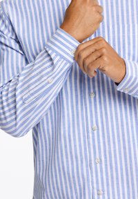 Lichtblauw en wit gestreept overhemd met lange mouwen, voorzien van een borstzak en knoopdetail aan de manchetten. Glad stofmateriaal.