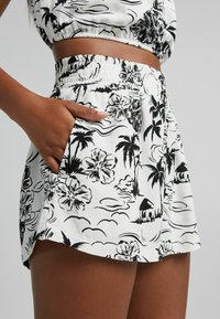 Kraťasy s černobílým květinovým potiskem a elastickým pasem, s bočními kapsami a volným střihem, které předvádějí tropický design.