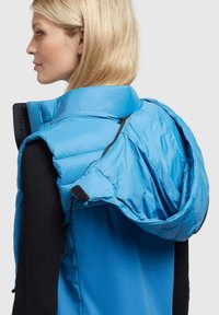 Blå puffer väst med hög krage, med en dragkedja på huvan och svart ribbat tyg på sidorna. Slät textur med en lätt design.