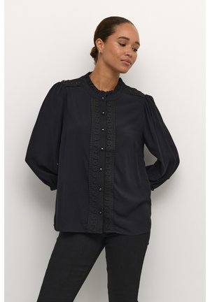 Blouse noire avec des bordures en dentelle raffinée le long de la patte de boutonnage, dotée d'un col à volants et de manches longues bouffantes. Texture de tissu lisse.