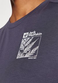 Marineblå bomull T-skjorte med hvit grafikk av en plante og merkevarenavn "Jack Wolfskin," med teksten "SINCE 1981."