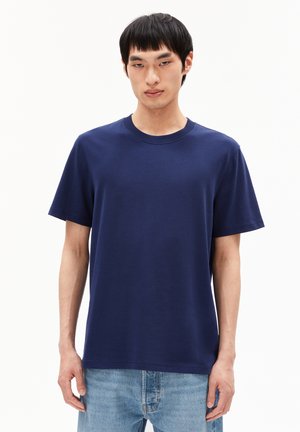Marineblaue Baumwoll-T-Shirt mit kurzen Ärmeln und rundem Ausschnitt. Glatte Textur und lockere Passform, kombiniert mit hellblauen Jeans.