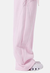 Pantalones de chándal rosas hechos de una tela suave, con costuras blancas, un corte holgado y puños ajustados, combinados con zapatos grises.