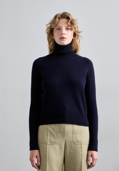 Navyblauer Rollkragenpullover mit geripptem Halsausschnitt und Saum, gefertigt aus weichem Strickmaterial, kombiniert mit leicht strukturierten Hosen.