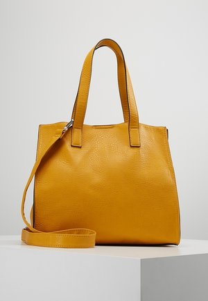 Gelbe Lederhandtasche mit zwei oberen Griffen und einem abnehmbaren Schulterriemen, präsentiert auf einem weißen Sockel vor einem hellgrauen Hintergrund.