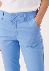 Pantalon en coton bleu clair avec une coupe standard, doté d’une couture plate à l’avant, de poches latérales et de détails de couture subtils.