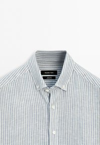 Light blue and white vertical striped linen shirt with button-down collar, visible brand label, and front buttons.
