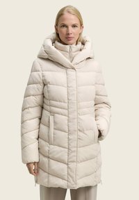 Doudoune beige clair, avec un col montant, une capuche, un motif matelassé diagonal, une fermeture éclair à l'avant et des poches latérales. Texture douce et lisse.