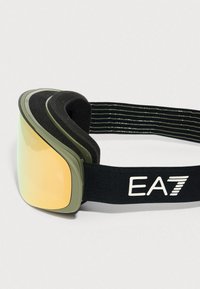 Gogle narciarskie z żółtymi, refleksyjnymi soczewkami, oliwkowo-zieloną oprawką oraz czarnym elastycznym paskiem z białym logo „EA7”.
