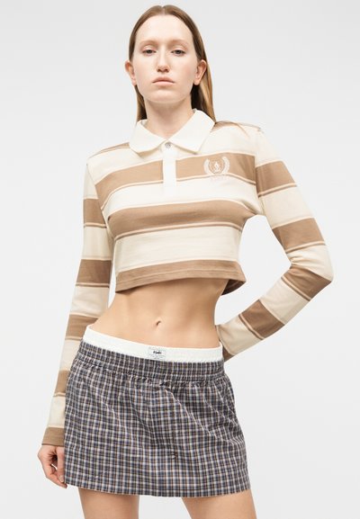 Γυναίκα που φοράει cropped πόλο με μακρυά μανίκια σε μπεζ και άσπρες ρίγες και μίνι φούστα καρό μπλε.